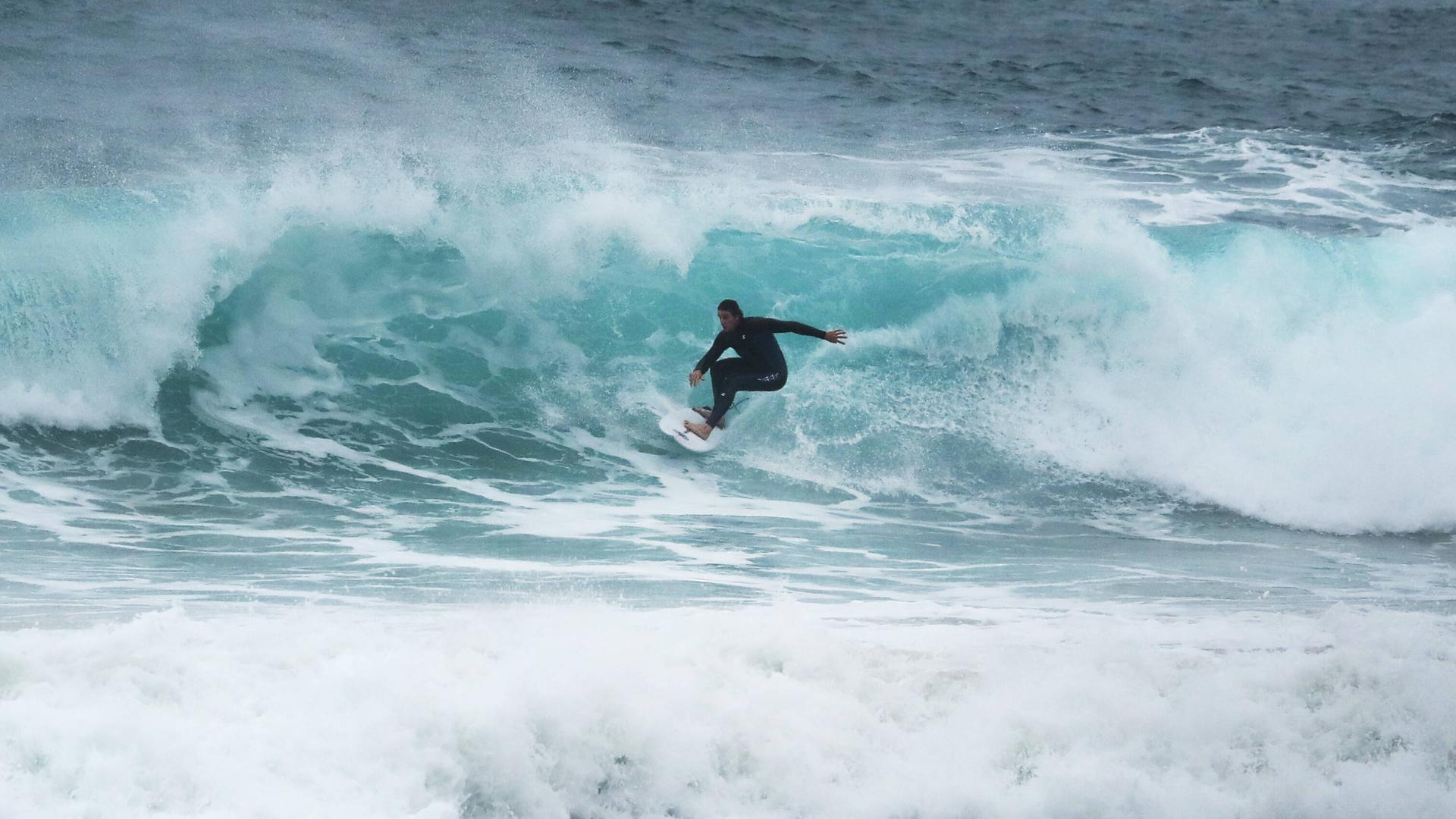 Auf dem Bild ist ein Surfer zu sehen, der über eine Welle reitet. 