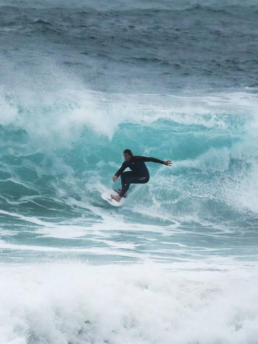 Auf dem Bild ist ein Surfer zu sehen, der über eine Welle reitet. 