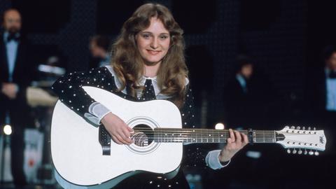 Nicole in einem weiß-gepunkteten Kleid und mit einer weiteren Gitarre.