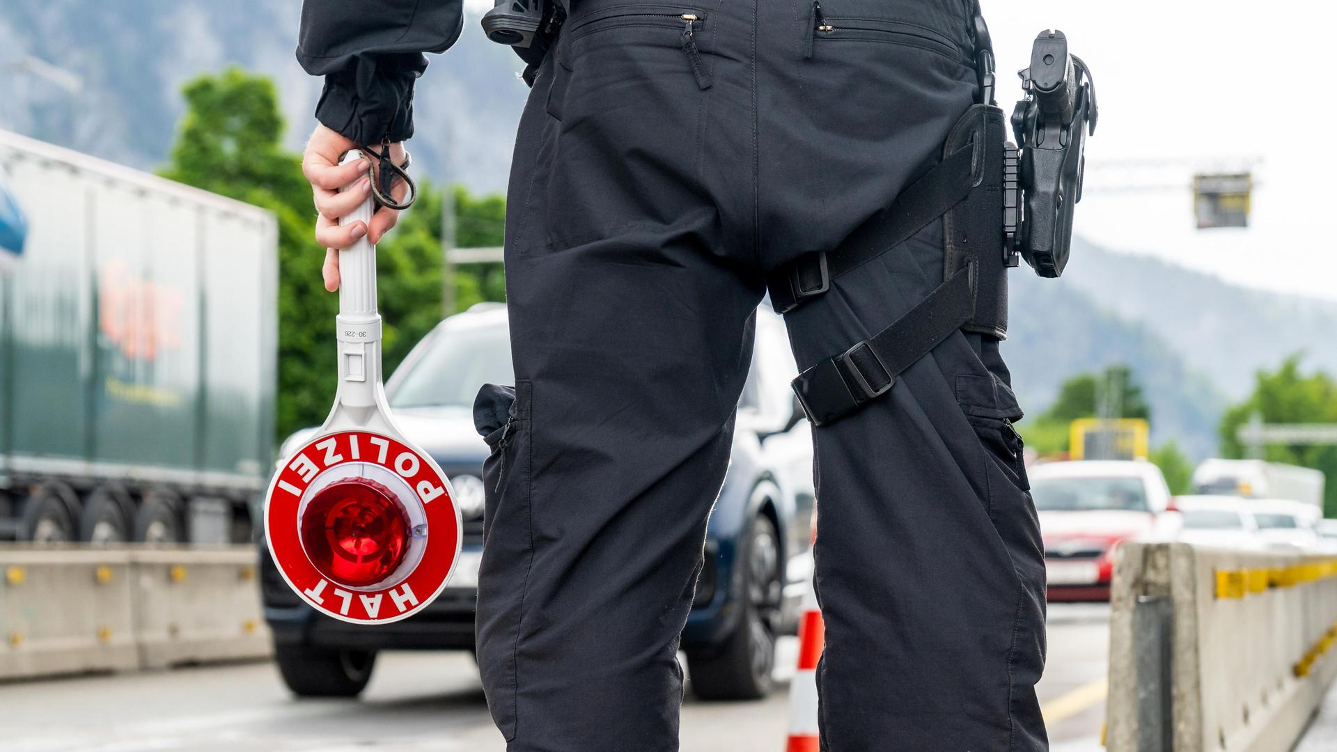 Ein Polizist hält eine Kelle mit Aufschrift: HALT POLIZEI an der Autobahn Ein Polizist hält eine Kelle mit Aufschrift: HALT POLIZEI an der Autobahn