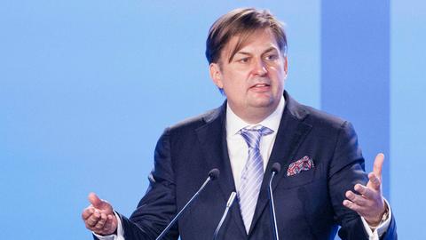 Krah mit Krawatte und Einstecktuch im dunklen Jackett steht mit beiden Händen gestikulierend am Rednerpult. Hinterihmn eine Wabnd in zwei verschiedenen Blautönen.