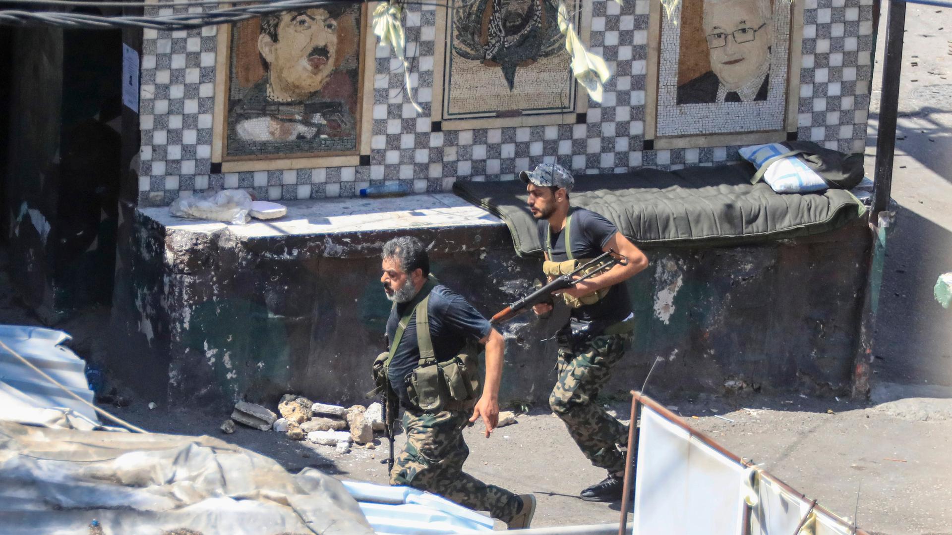 Zwei bewaffnete Männer laufen in Tarnkleidung durch eine schmale Gasse. An der Wand hinter ihnen ist unter anderem ein Bild von Palästinenserpräsident Mahmud Abbas zu sehen. Zwei bewaffnete Männer laufen in Tarnkleidung durch eine schmale Gasse. An der Wand hinter ihnen ist unter anderem ein Bild von Palästinenserpräsident Mahmud Abbas zu sehen.
