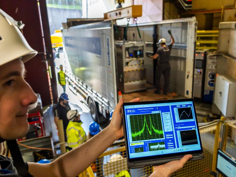 Ein Wissenschaftler am CERN zeigt einen Bildschirm, auf dem Antimateriemenge zu sehen ist in Form von Kurven. Im Hintergrund wird eine Box in einen LKW eingeladen. Europäische Organisation für Kernforschung in Genf im März 2026 Ein Wissenschaftler am CERN zeigt einen Bildschirm, auf dem Antimateriemenge zu sehen ist in Form von Kurven. Im Hintergrund wird eine Box in einen LKW eingeladen. Europäische Organisation für Kernforschung in Genf im März 2026