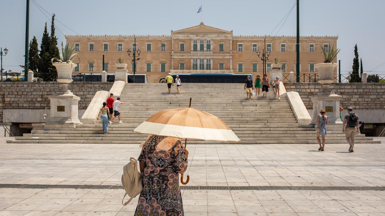 Griechenland, Athen: Eine Frau schützt sich mit einem Sonnenschirm vor der Sonne, während sie auf dem Syntagma-Platz im Zentrum von Athen spaziert.