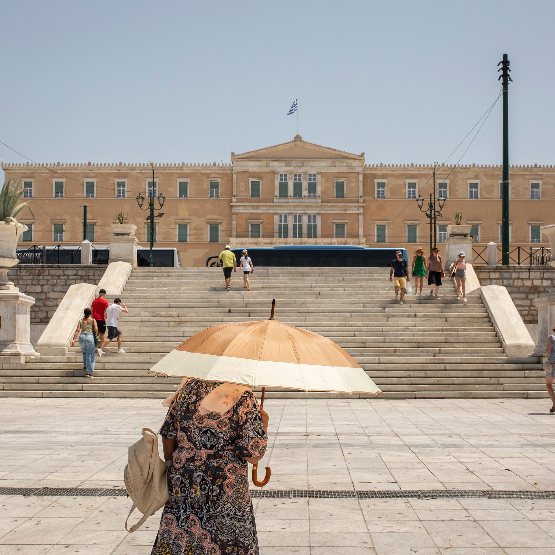 Griechenland, Athen: Eine Frau schützt sich mit einem Sonnenschirm vor der Sonne, während sie auf dem Syntagma-Platz im Zentrum von Athen spaziert.