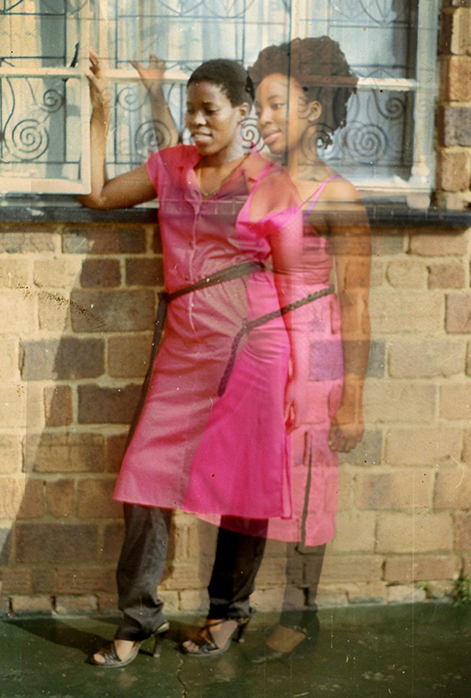 Doppelbelichtung zweier schwarzer Frauen, die das gleiche rosa Kleid tragen. Sie stehen vor einem Haus und halten sich am Fensterrahmen fest.