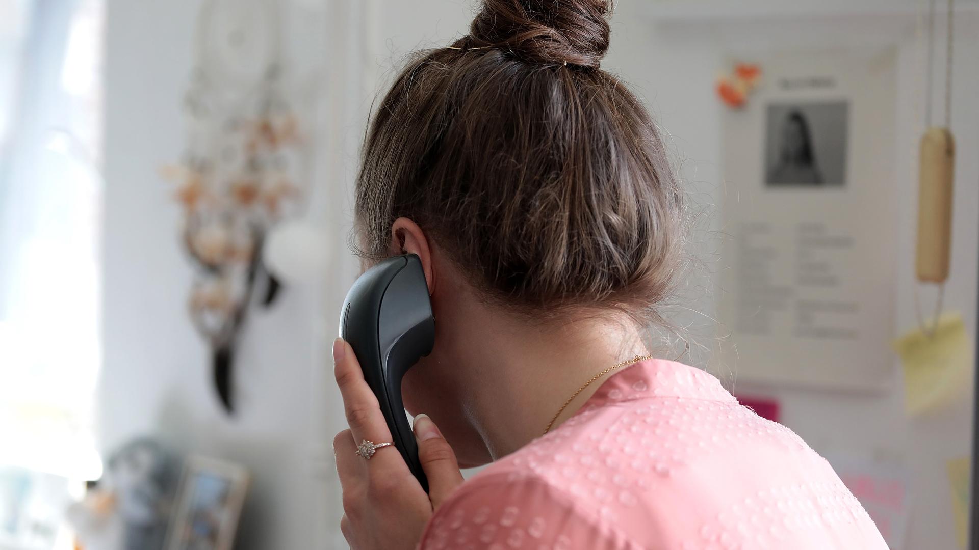 Rückansicht einer Frau mit zum Dutt aufgestecktem Haar, die am Schreibtisch sitzt und ein Telefonat führt. 