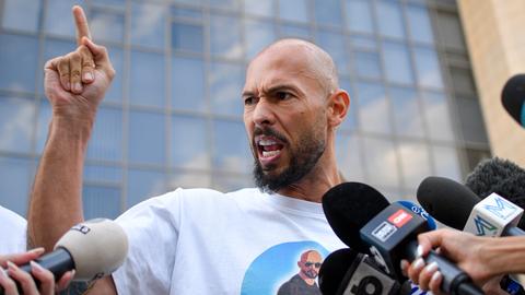 Andrew Tate gestikuliert wild vor Pressevertretern. Im Hintergrund ist ein Gerichtsgebäude zu sehen Andrew Tate gestikuliert wild vor Pressevertretern. Im Hintergrund ist ein Gerichtsgebäude zu sehen