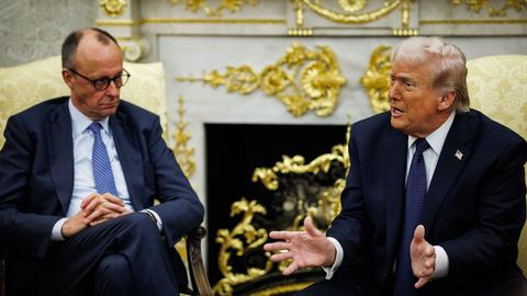 Bundeskanzler Friedrich Merz sitzt neben US-Präsident Donald Trump, der gerade spricht und gestikuliert, in goldenen Sesseln vor einem goldbeschlagenen Kamin im Oval Office im Weißen Haus in Washington.  