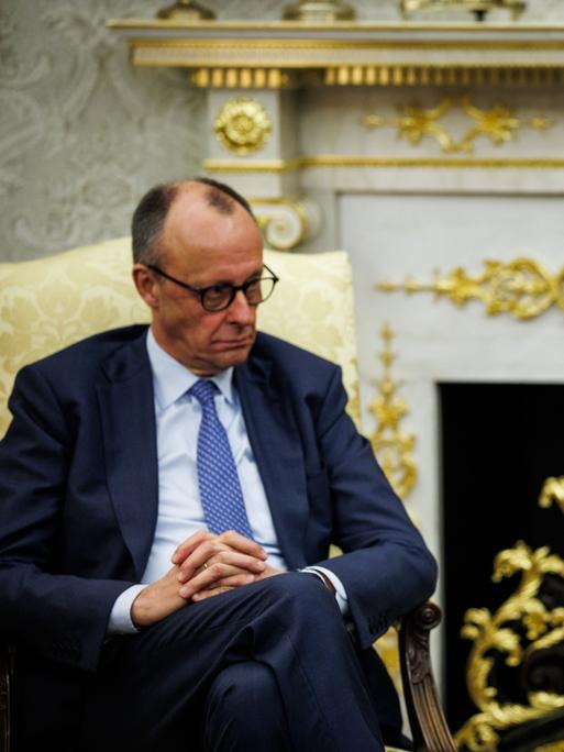 Bundeskanzler Friedrich Merz sitzt neben US-Präsident Donald Trump, der gerade spricht und gestikuliert, in goldenen Sesseln vor einem goldbeschlagenen Kamin im Oval Office im Weißen Haus in Washington.  