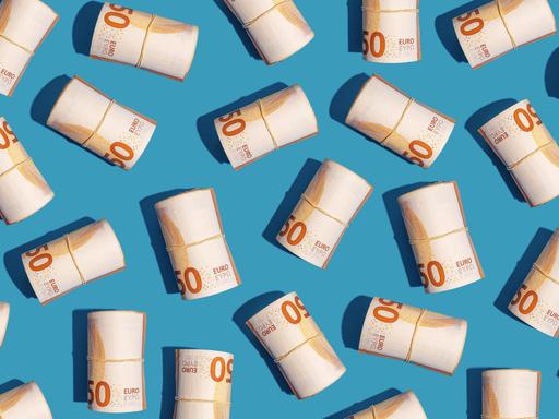 Mehrere Rollen mit 50-Euro-Scheinen liegen auf einem hellblauen Untergrund
