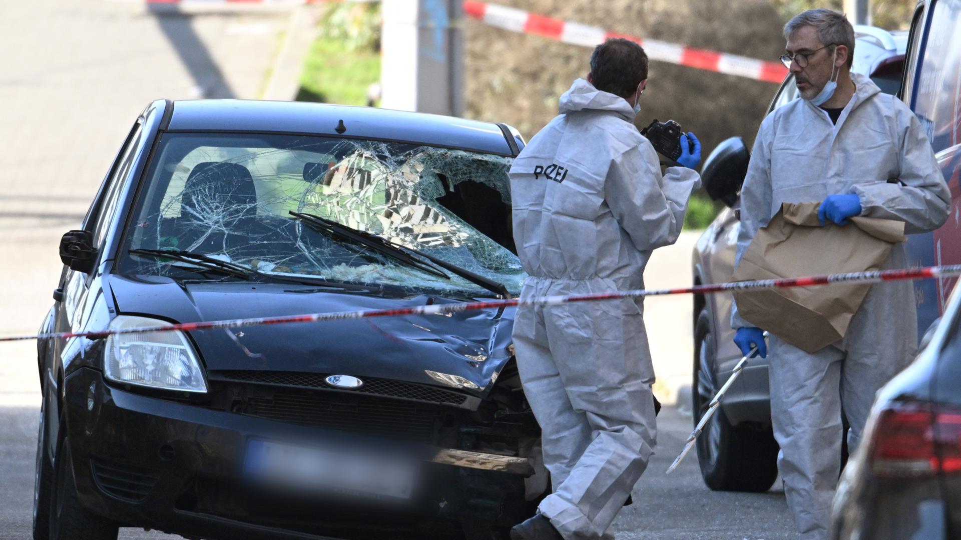 Beamte der Spurensicherung untersuchen ein beschädigtes Fahrzeug an einer Zufahrt zur Rheinbrücke. 