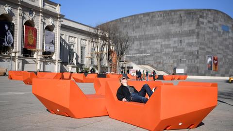 Eine Frau sonnt sich in einem Sitzmöbel im Außenbereich des MuseumsQuartierin Wien. Im Hintergrund Eine Frau sonnt sich in einem Sitzmöbel im Außenbereich des MuseumsQuartierin Wien. Im Hintergrund