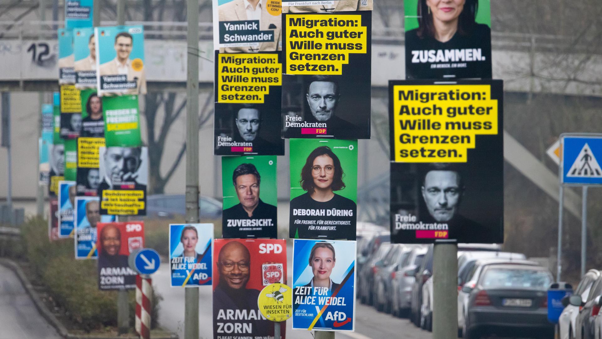 Wahlplakate der etablierten Parteien CDU, AfD, Bündnis 90/Die Grünen, SPD und FDP hängen im Frankfurter Nordwesten an mehreren Laternenmasten. Auf einem Plakat der FDP steht "Migration: Auch guter Wille muss Grenzen haben".