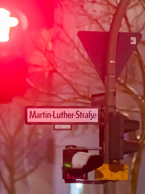 Das Straßenschild der Martin-Luther-Straße in Berlin-Schöneberg im Dunklen im Winter. Schnee liegt auf einer Ampel, eine andere zeigt rot.