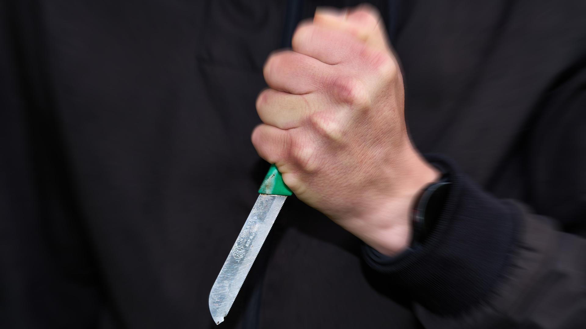 Ein schwarz gekleideter Mann hält ein Messer mit fester Faust. Ein schwarz gekleideter Mann hält ein Messer mit fester Faust.