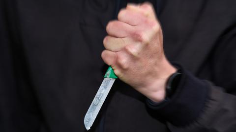 Ein schwarz gekleideter Mann hält ein Messer mit fester Faust. 