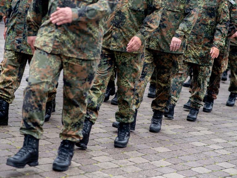 Zu sehen sind die Beine mehrerer Bundeswehr-Soldaten in Tarn-Uniform, die gerade marschieren.