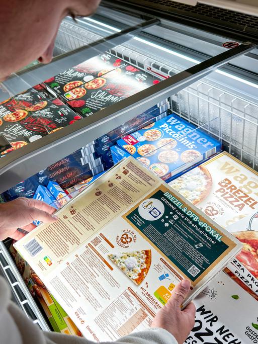 Ein Mann vergleicht im Supermarkt die Nährwertangaben einer Tiefkühlpizza. 