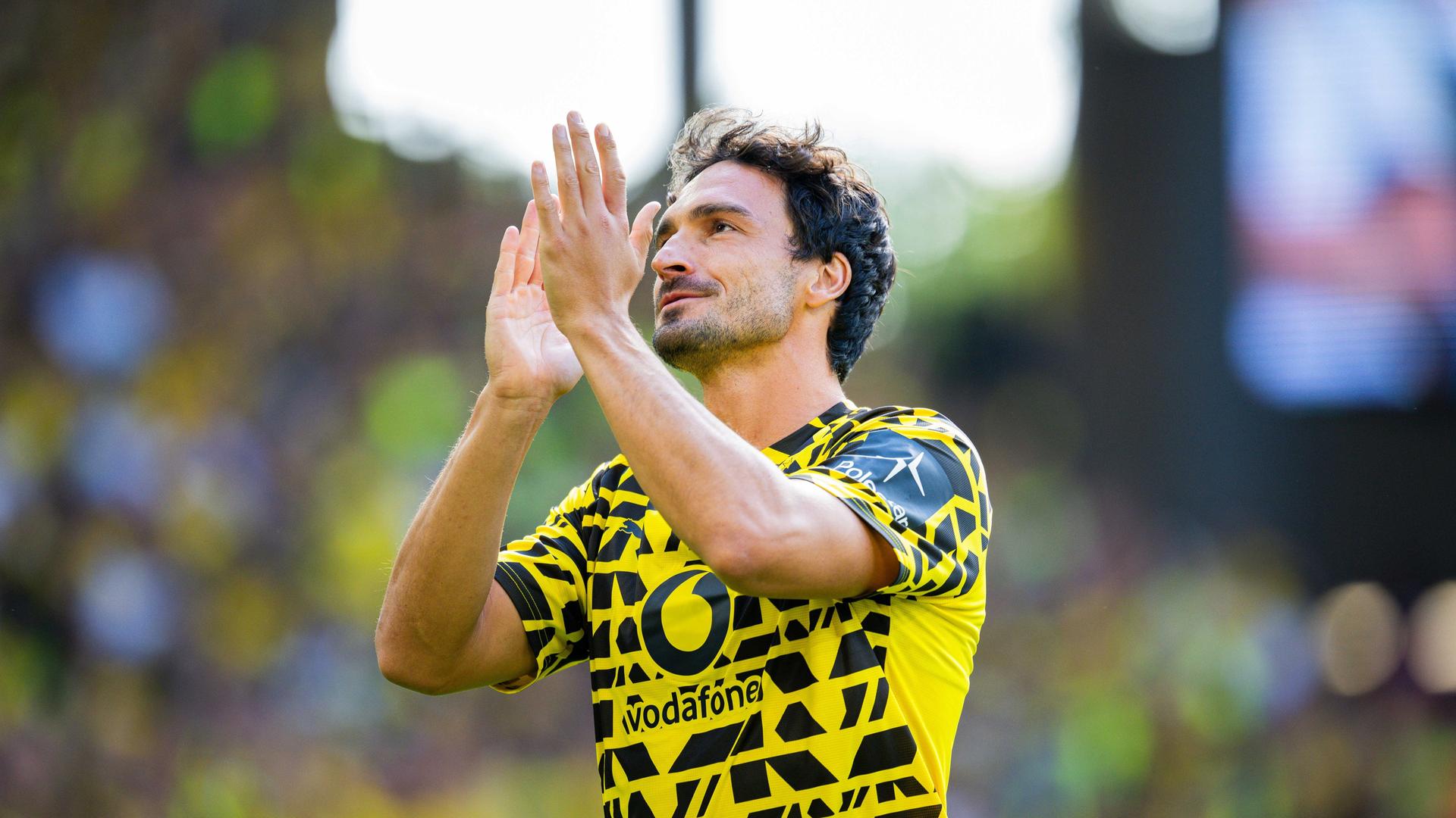 Der Fußballer Mats Hummels in einem gelb-schwarzen Trikot. Er hebt die Hände, um dem Publikum zu klatschen. Der Fußballer Mats Hummels in einem gelb-schwarzen Trikot. Er hebt die Hände, um dem Publikum zu klatschen.