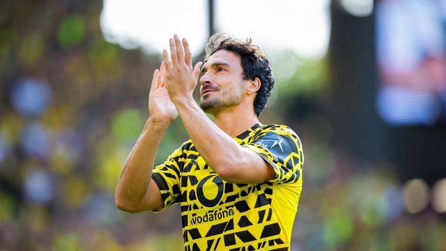 Der Fußballer Mats Hummels in einem gelb-schwarzen Trikot. Er hebt die Hände, um dem Publikum zu klatschen. 