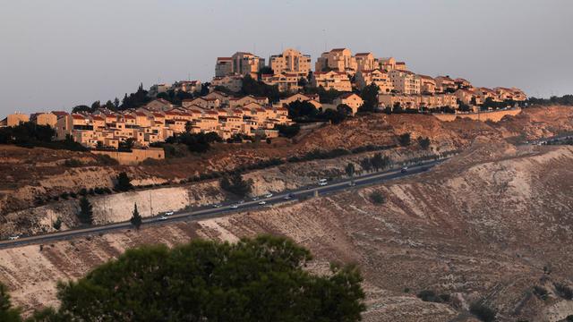 Autos fahren auf einer Straße unterhalb einer großen Siedlung moderner Häuser entlang. Es ist eine israelische Siedlung außerhalb von Jerusalem im Westjordanland.