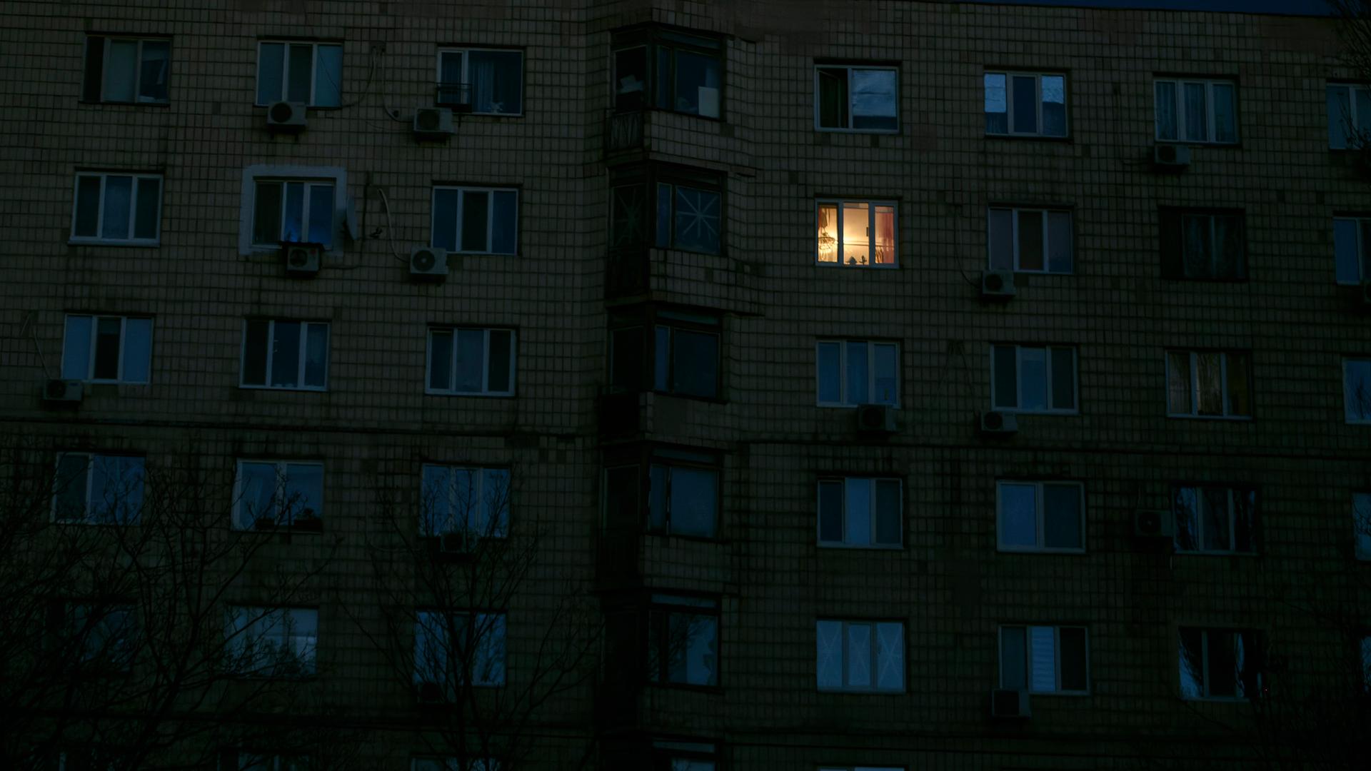 In einem dunklen Mehrfamilienhaus brennt das Licht in einem Zimmer.