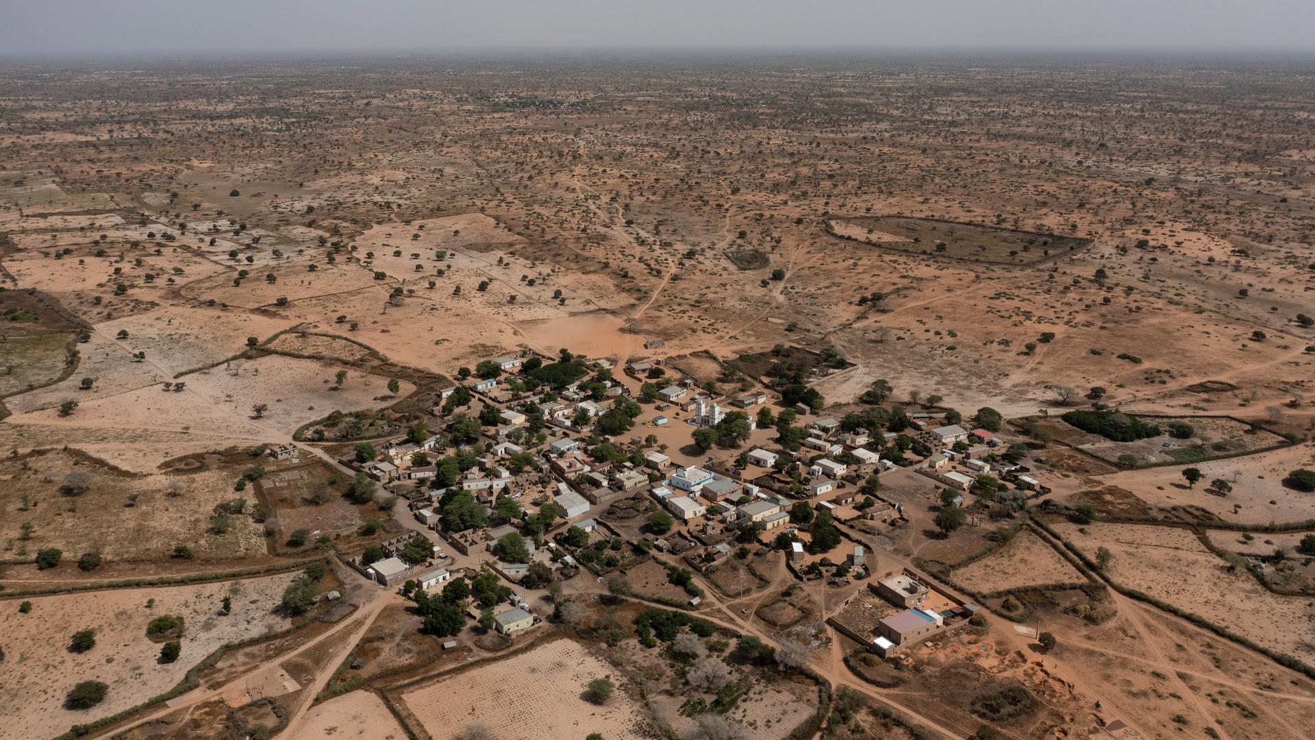 Luftaufnahme eines Dorfes in der Sahelzone. Zu sehen sind Häuser, Bäume und Wege, die sich durch das Dorf und die umliegende Landschaft ziehen.