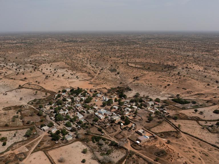 Luftaufnahme eines Dorfes in der Sahelzone. Zu sehen sind Häuser, Bäume und Wege, die sich durch das Dorf und die umliegende Landschaft ziehen.