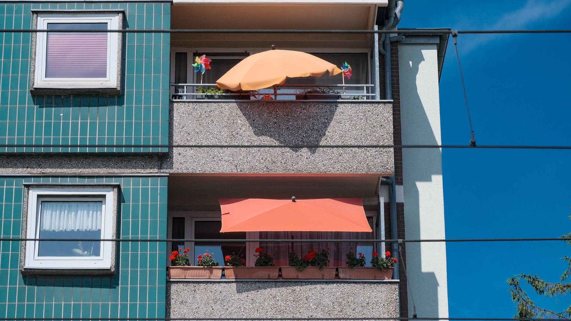 Plattenbau mit zwei begrünten Balkonen mit Sonnenschirmen