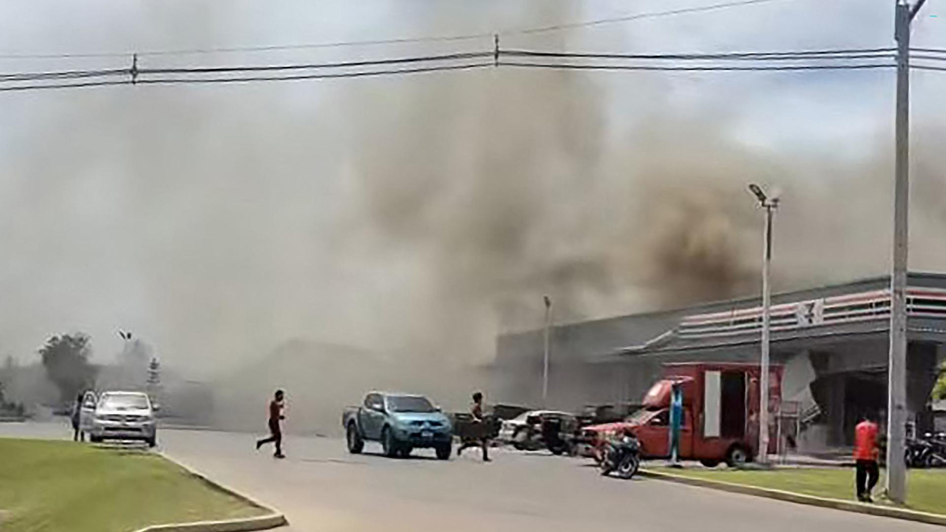 Von einem Lebensmittelgeschäft und einer Tankstelle steigt nach einem kamboschanischen Raketenangriff Rauch auf. Menschen laufen über die Straße.