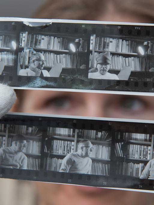 Andrea Werner, Mitarbeiterin im Wolfgang-Koeppen-Archiv (WKA) des Instituts für Deutsche Philologie an der Ernst-Moritz-Arndt Universität Greifswald, hält Kontaktabzüge von Wolfgang Koeppen in die Kamera. Sie trägt weiße Handschuhe, ihre Augen sind zwischen den Fotos zu sehen.