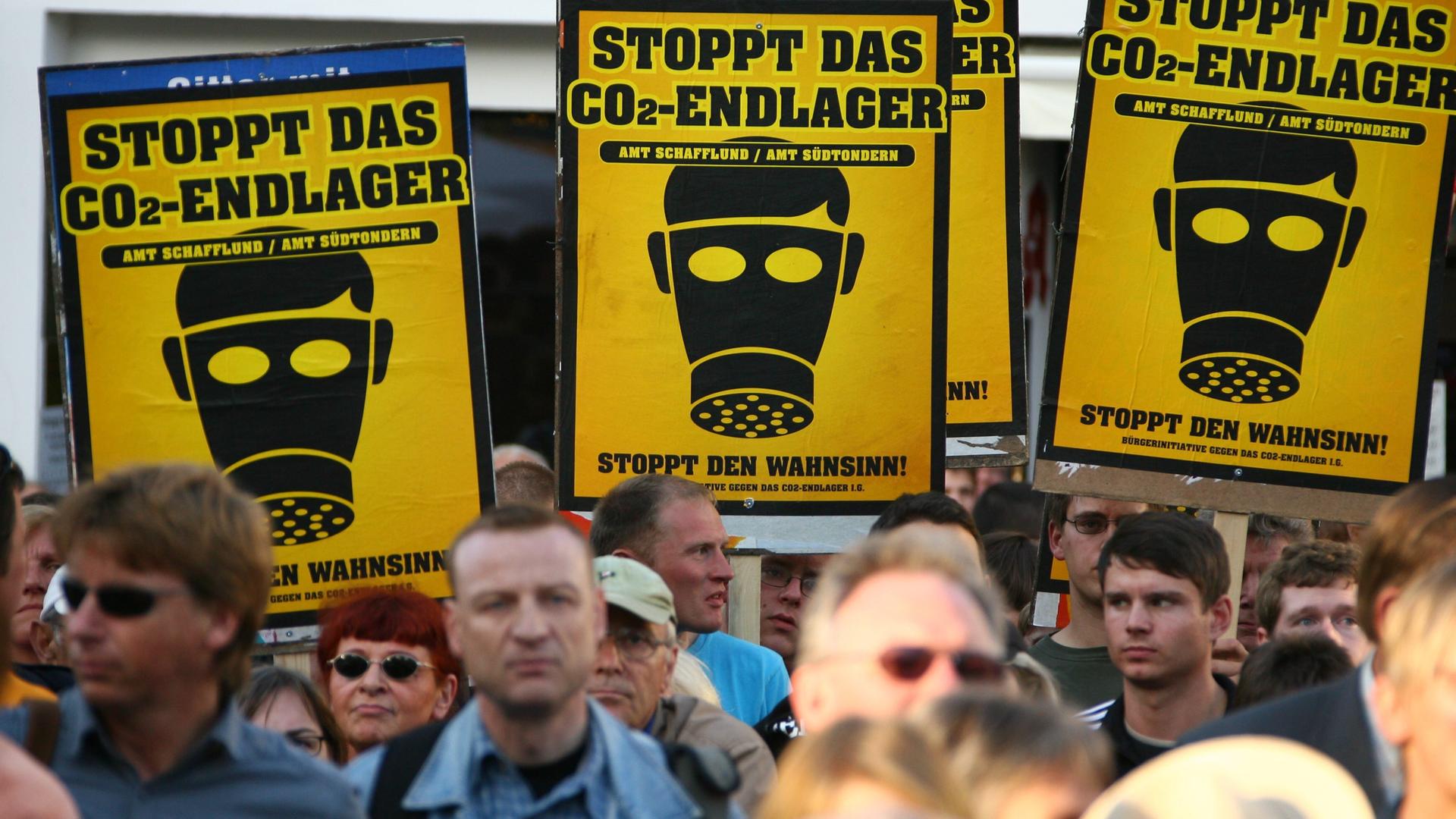 Demonstranten tragen gelbe Schilder, auf denen schwarze Gasmasken und die Aufschrift "Stoppt das CO2-Endlager" aufgedruckt sind.