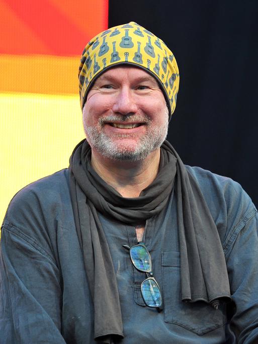 Das Bild zeigt den Comiczeichner Ingo Römling, vom Kopf bis zum Unterbauch. Er lächelt, trägt einen schwarzen Schal und eine gelbe Mütze. 