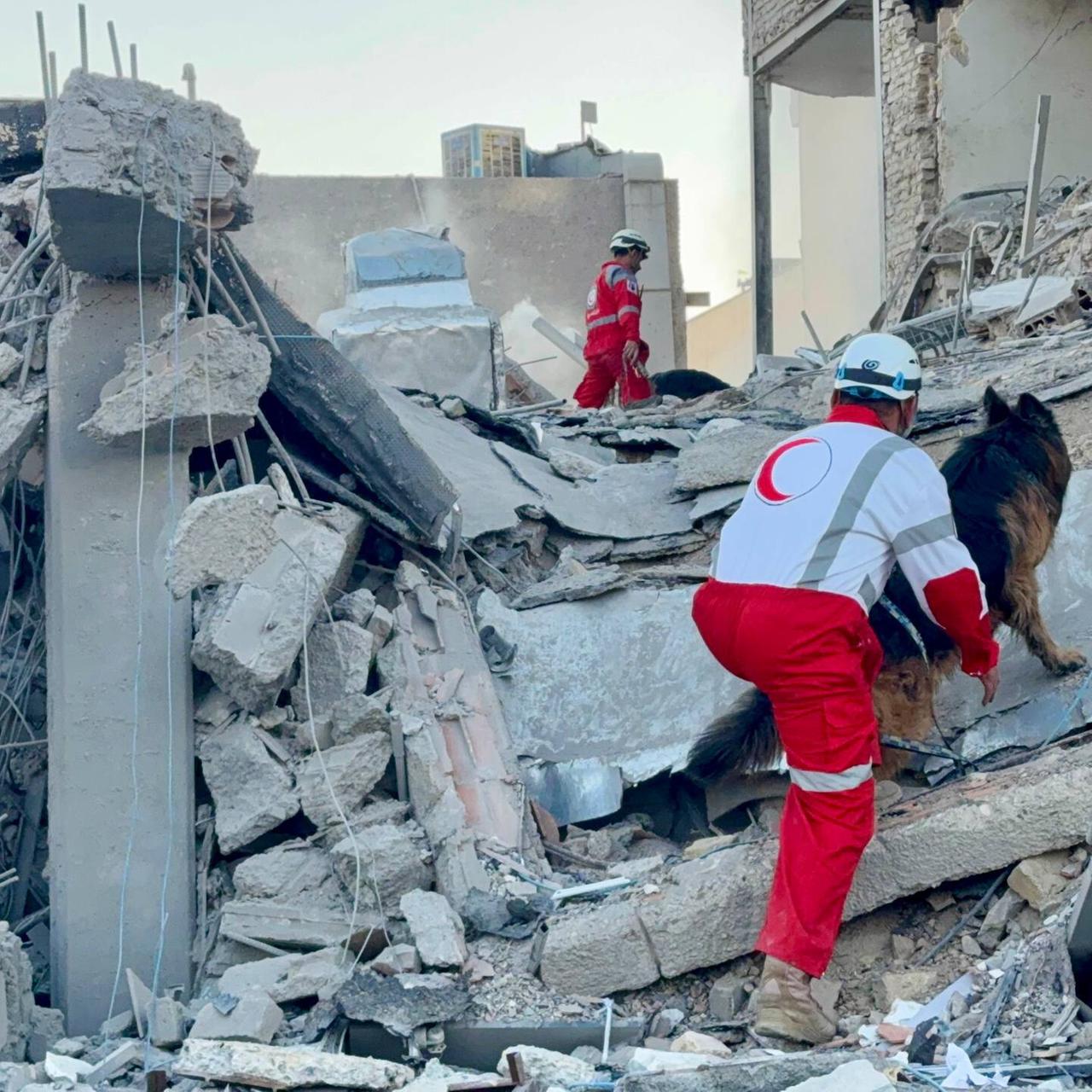 Mitglieder der Rettungsmannschaften der Iranischen Rothalbmondgesellschaft stehen auf Trümmern. Sie arbeiten an der Stelle eines Gebäudes, das bei einem Luftangriff im Iran beschädigt wurde.