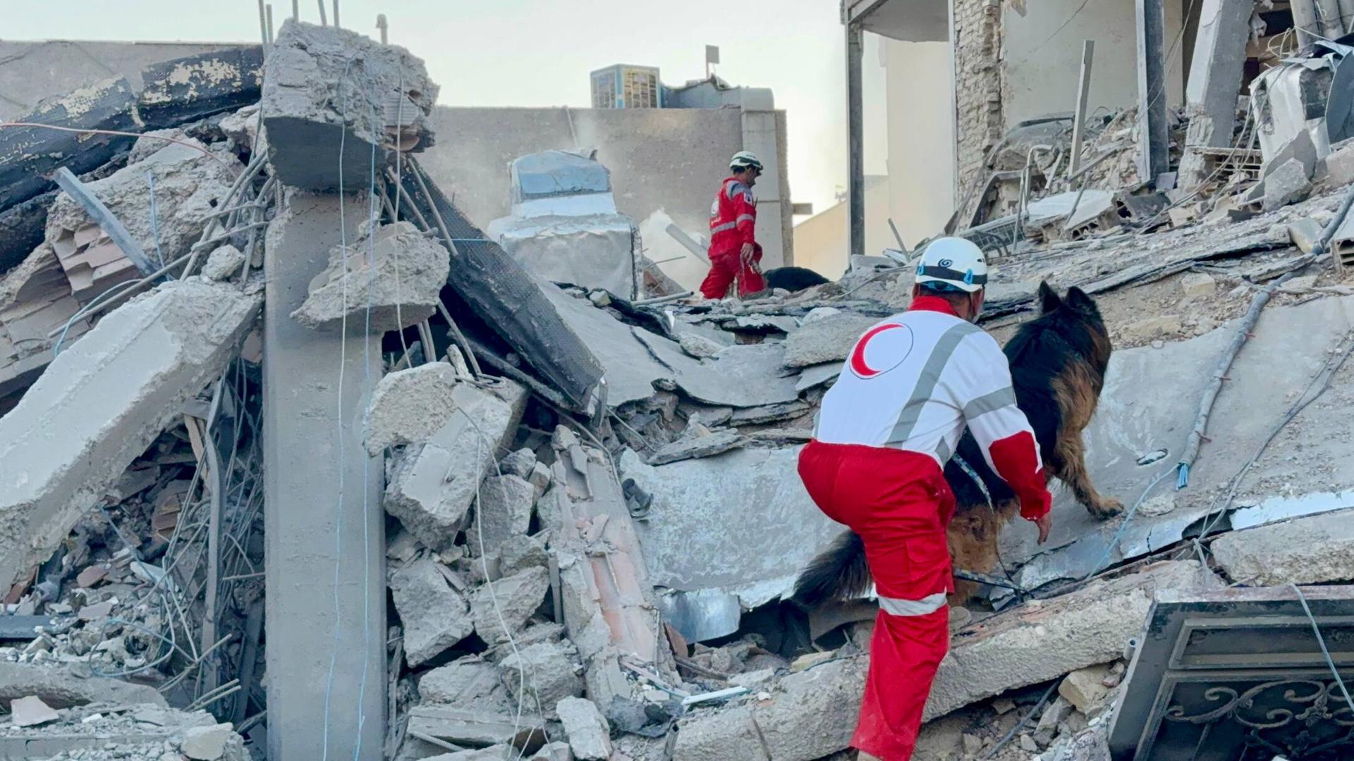 Rettungskräfte der Iranischen Rothalbmondgesellschaft stehen auf Trümmern. Sie arbeiten an der Stelle eines Gebäudes, das bei einem Luftangriff im Iran beschädigt wurde.