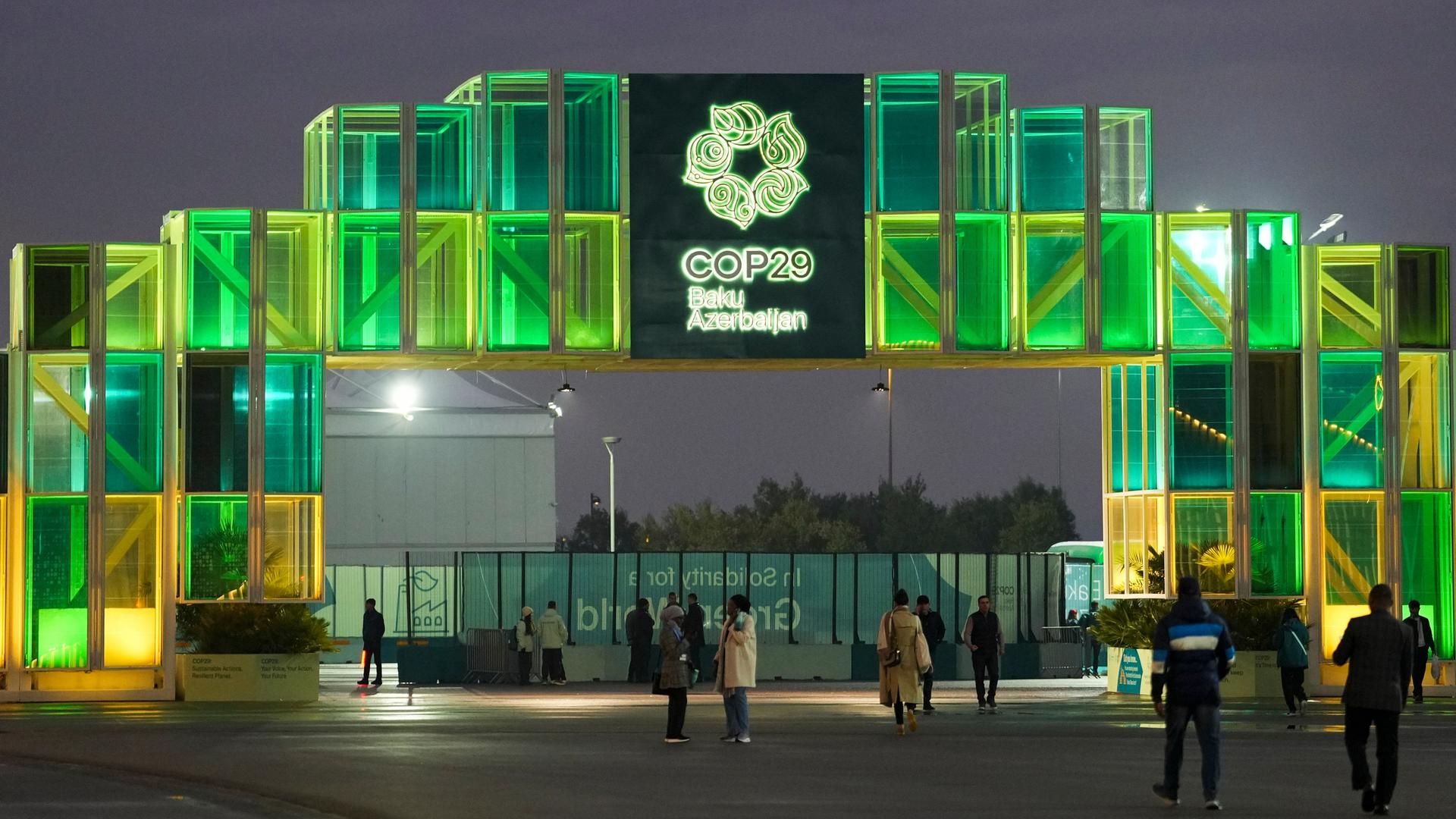 Menschen gehen am Eingang der Weltklimakonferenz in Baku vorbei.