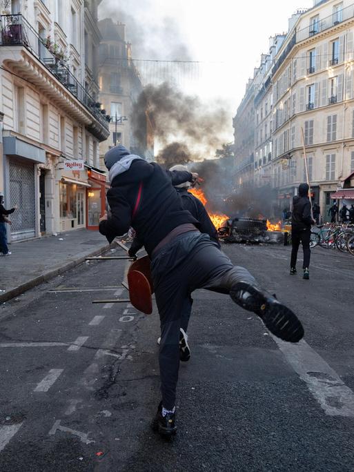 Ein gewalttätiger Demonstrant wirft eine Flasche in Richtung einiger Polizisten hinter einer brennenden Barrikade auf einer Straße in Paris. Ein gewalttätiger Demonstrant wirft eine Flasche in Richtung einiger Polizisten hinter einer brennenden Barrikade auf einer Straße in Paris.