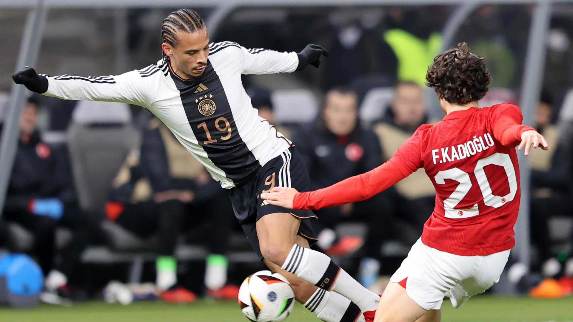 Ein deutscher Fußball-Spieler dribbelt mit dem Ball und wird von einem türkischen Gegenspieler gestört.