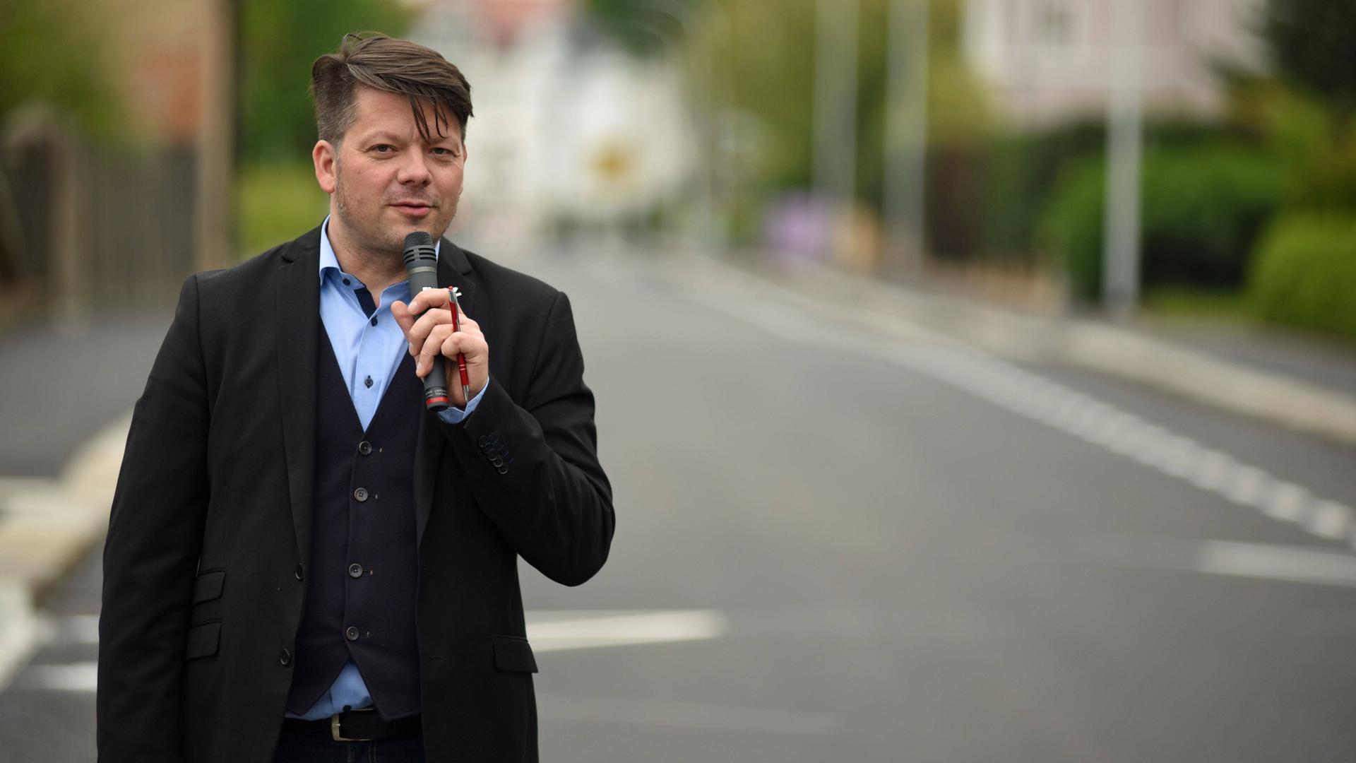 Der Zittauer Oberbürgermeister Thomas Zenker steht mit Mikrofon in der Hand auf einer Straße.