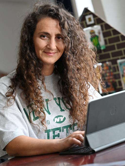 Lale Öztürk, eine Frau mit langen, lockigen Haaren, arbeitet an einem iPad. Sie koordiniert die Sprachförderung der Stadt Duisburg, macht Comedy und liest Menschen ehrenamtlich vor.