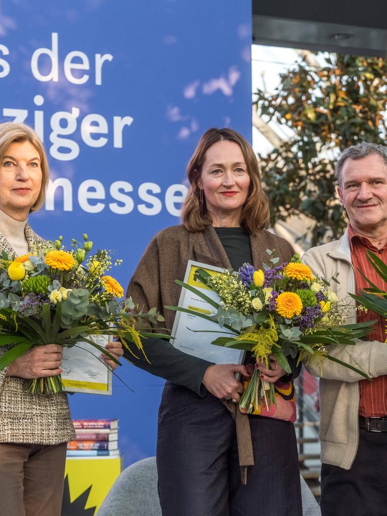 Die drei Buchpreisträger der Leipziger Buchmesse 2026 stehen mit Urkunden und Blumensträußen auf einer Bühne.