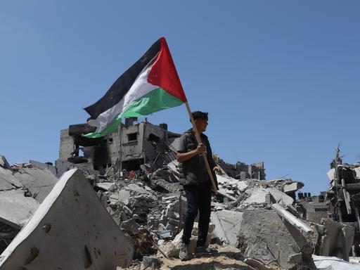 Ein Mann hält die Palästinenserfahne und steht auf einem Trümmerhaufen in Gaza. 