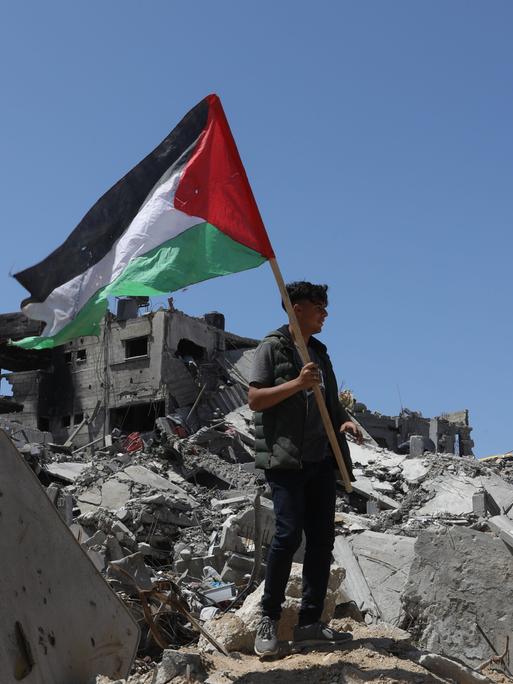 Ein Mann hält die Palästinenserfahne und steht auf einem Trümmerhaufen in Gaza. 