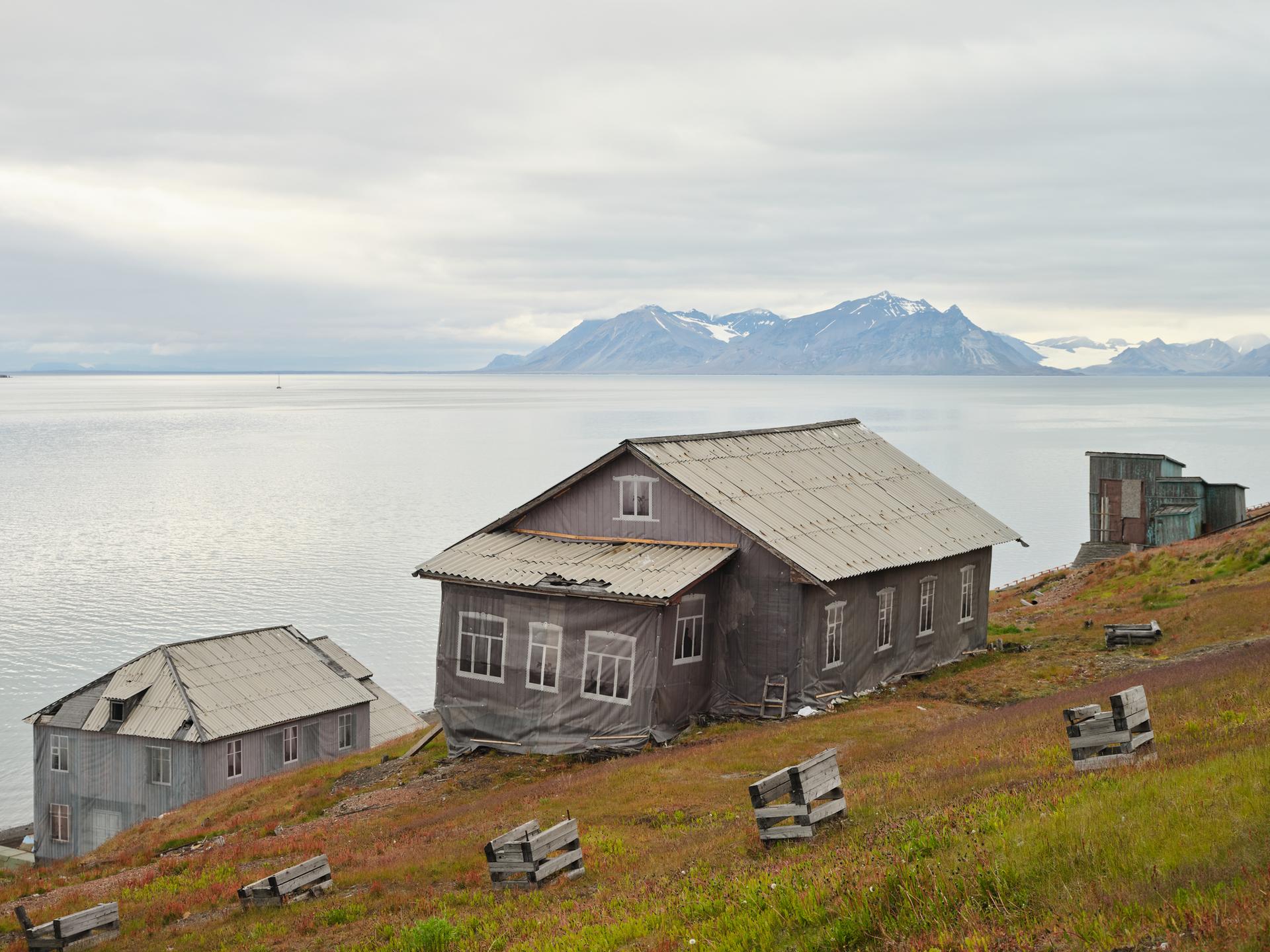 Häuser in Barentsburg, der russischen Siedlung auf Spitzbergen. Planen kaschieren den schleichenden Verfall. Im Hintergrund der Fjord und die Gletscher der Arktis.
