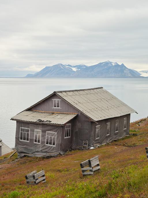 Häuser in Barentsburg, der russischen Siedlung auf Spitzbergen. Planen kaschieren den schleichenden Verfall. Im Hintergrund der Fjord und die Gletscher der Arktis.
