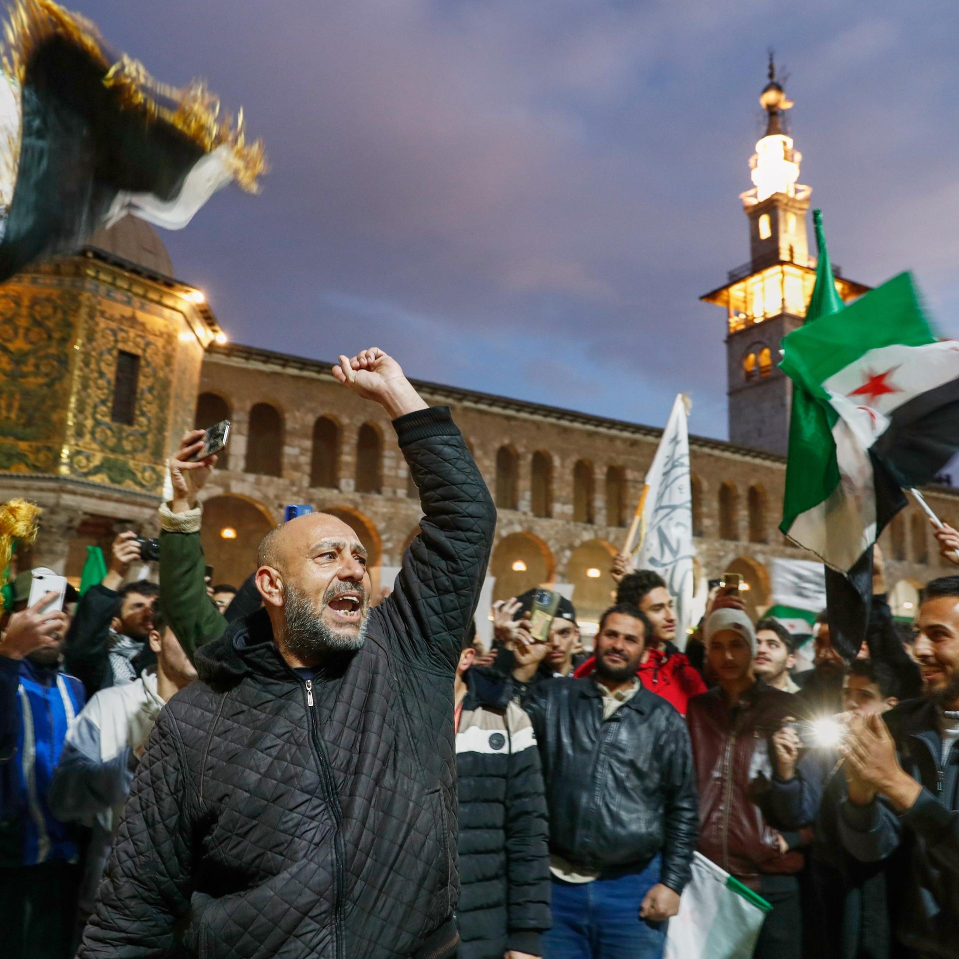 Damaskus: Syrer rufen Slogans und schwenken Fahnen vor der Umayyad-Moschee vor einem Gebet im Vorfeld der Feierlichkeiten zum ersten Jahrestag des Sturzes des Regimes von Assad.