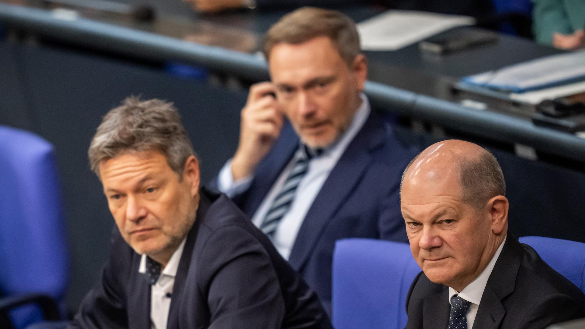 Olaf Scholz, Robert Habeck und Christian Lindner hören im Bundestag einer Rede zu.