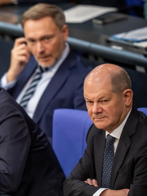 Olaf Scholz, Robert Habeck und Christian Lindner hören im Bundestag einer Rede zu.