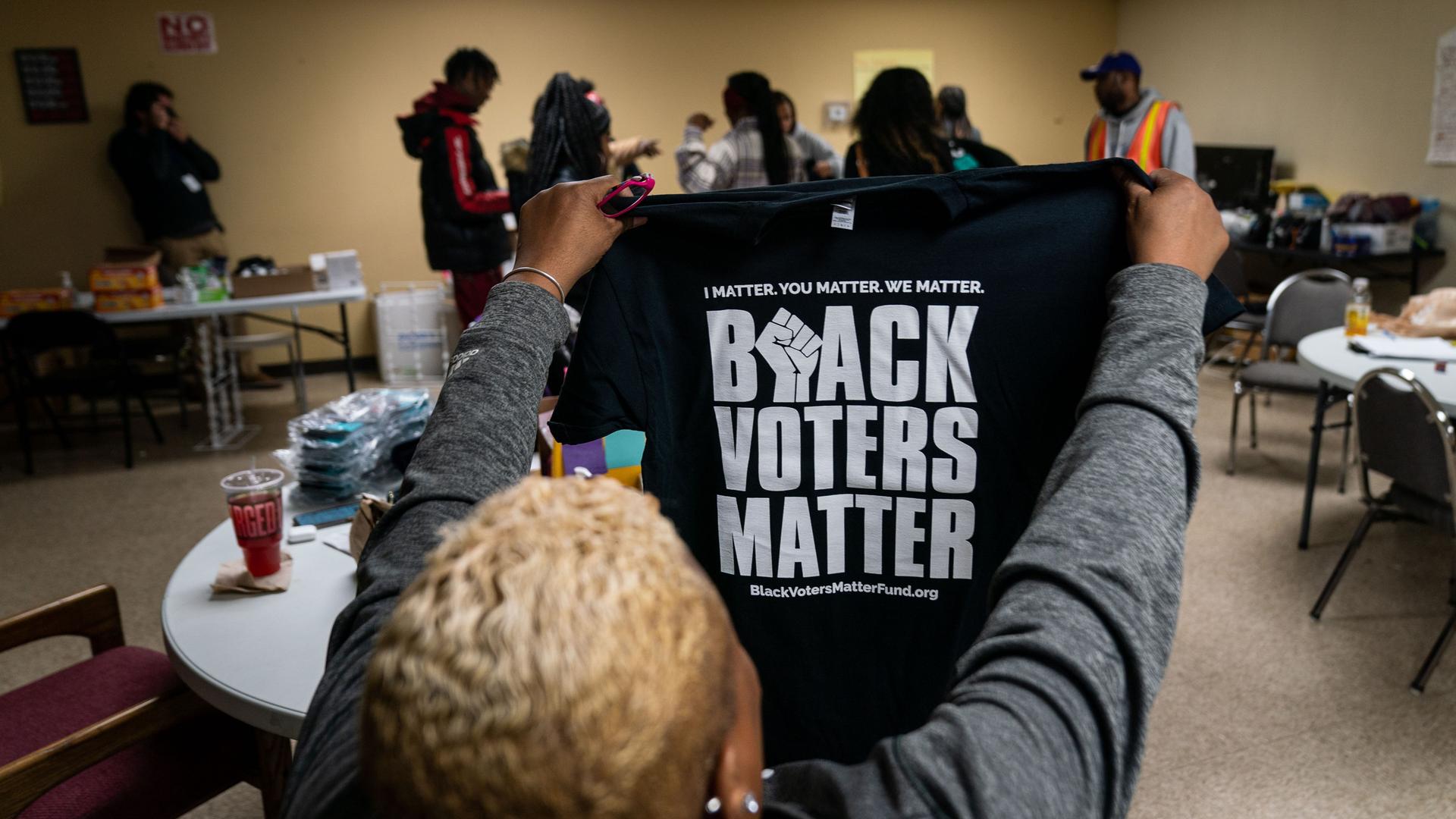 Eine Frau hält ein T-Shirt mit der Aufschrift "Black Voters Matter" in die Höhe.
